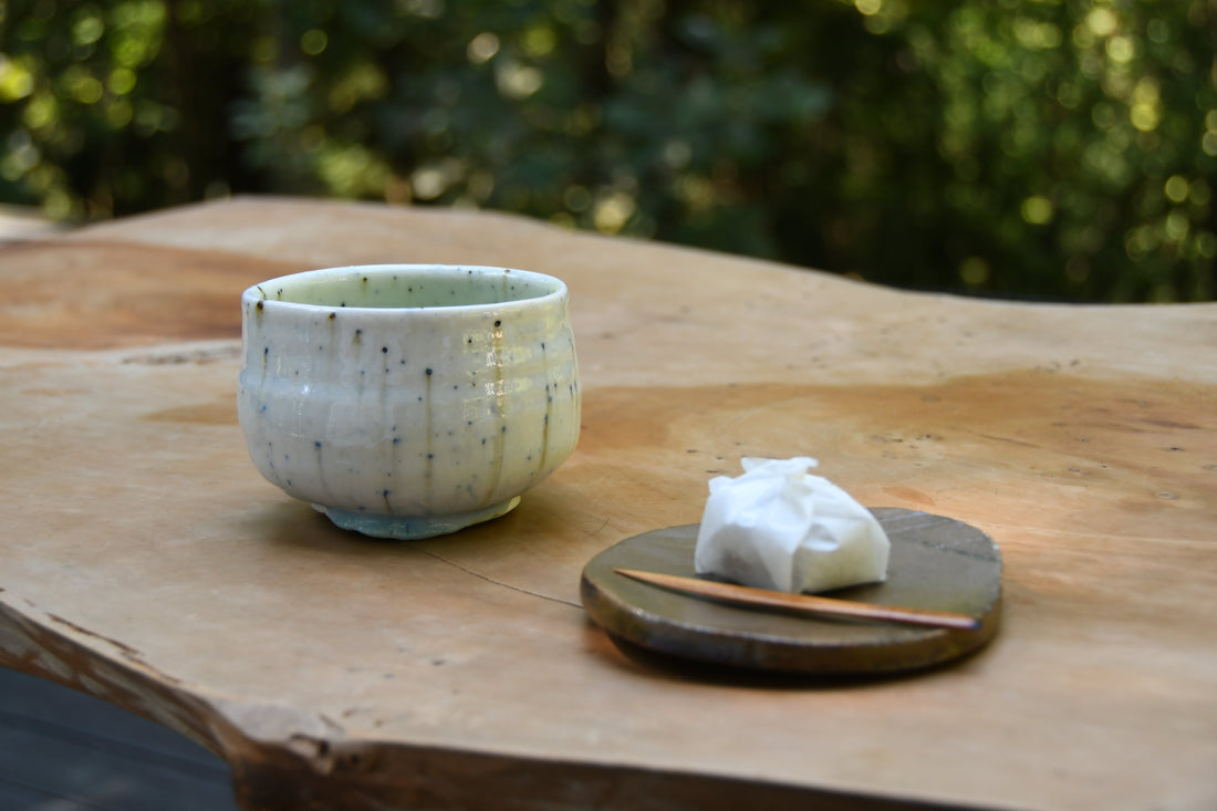 Handmade ash-glazed teacup by Hirohisa Kondo with traditional Japanese sweet on a wooden table