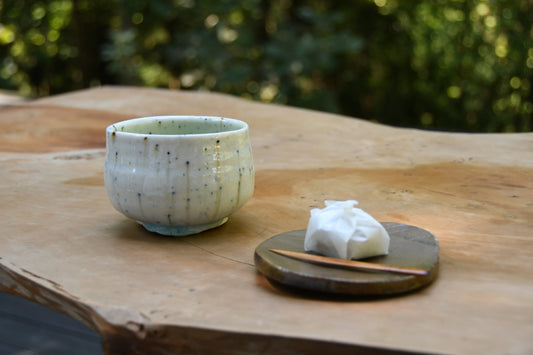 Handmade ash-glazed teacup by Hirohisa Kondo with traditional Japanese sweet on a wooden table