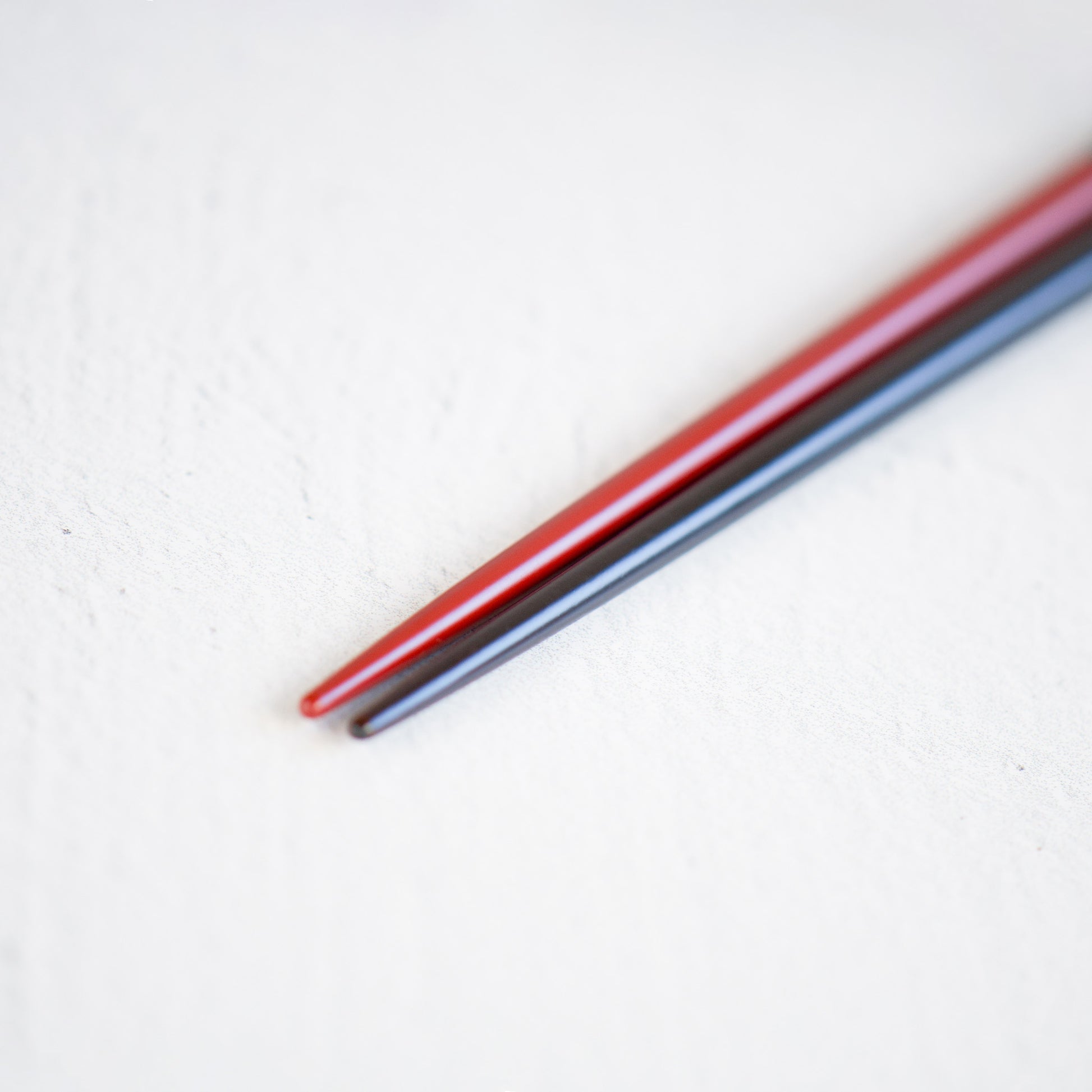 A detailed view of the finely crafted and pointed lacquered heads of the rouge and black chopsticks, designed for effortless and accurate food picking.