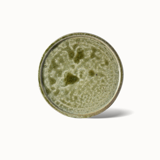 A round ceramic dinner plate with a rich, jewel-like green glaze and subtle textural patterns, displayed against a plain background.