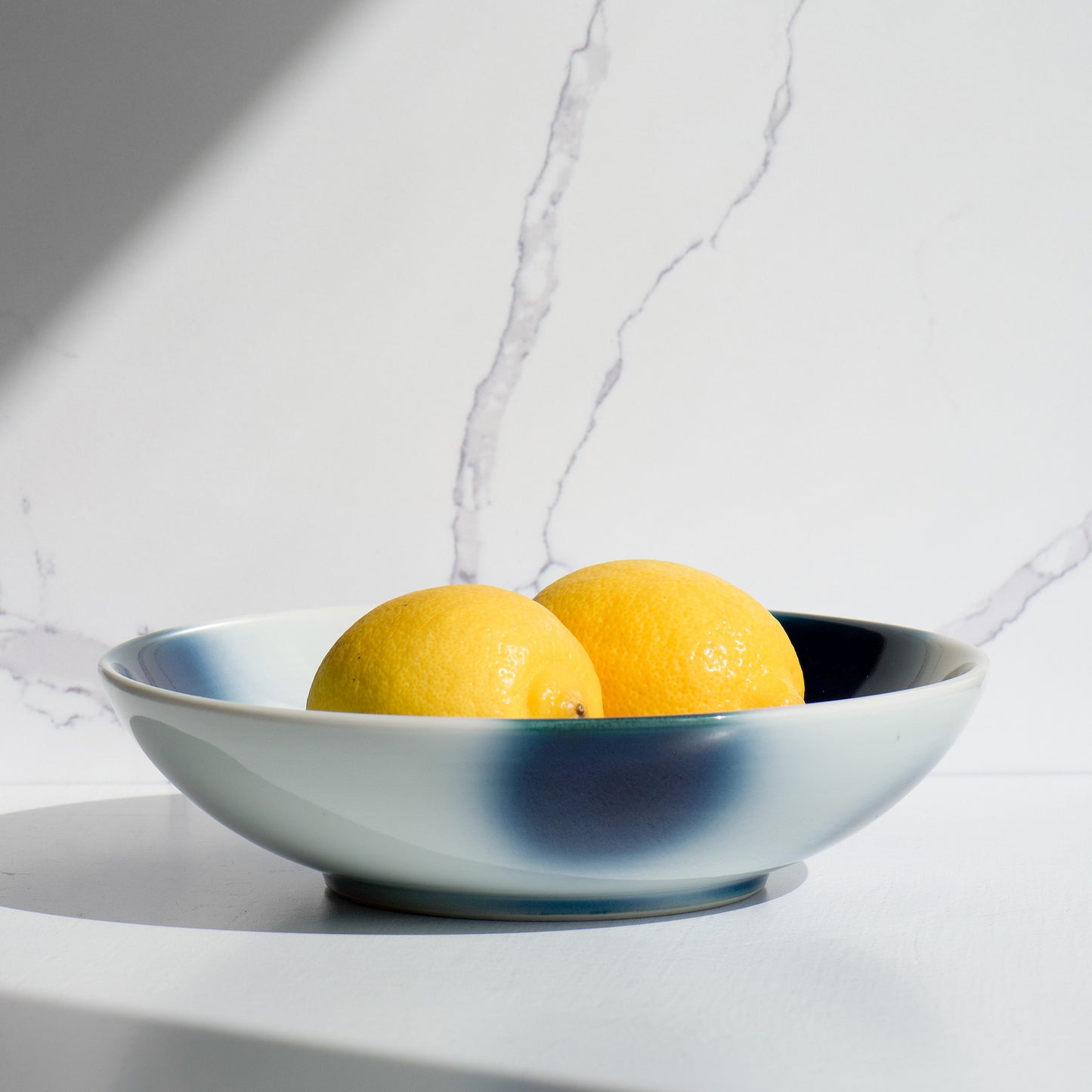 Mizu-oto pasta bowl styled with lemons under natural light on a marble background.