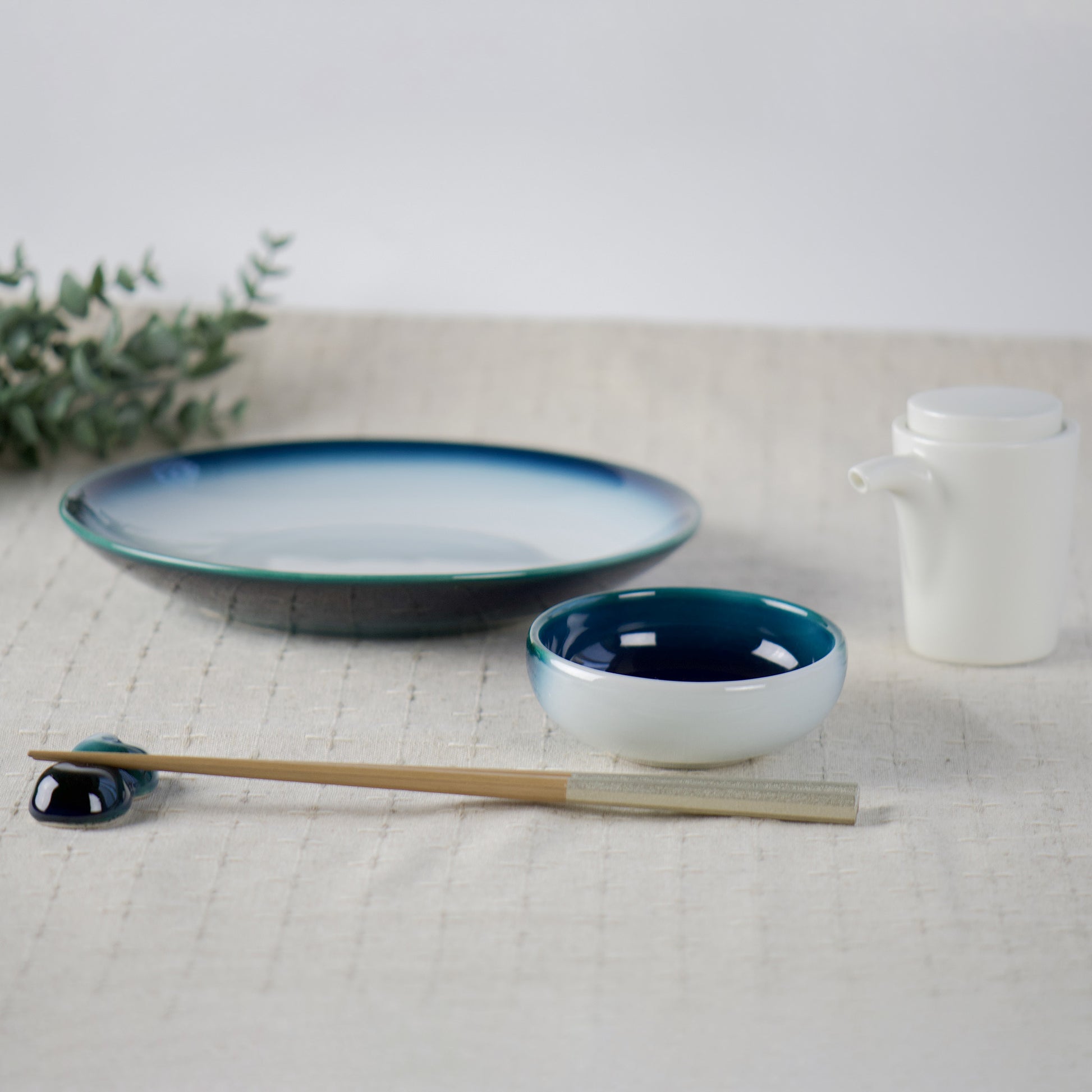 Seto Blue soy-sauce dish styled with matching plate, chopsticks and porcelain cruet on linen surface.