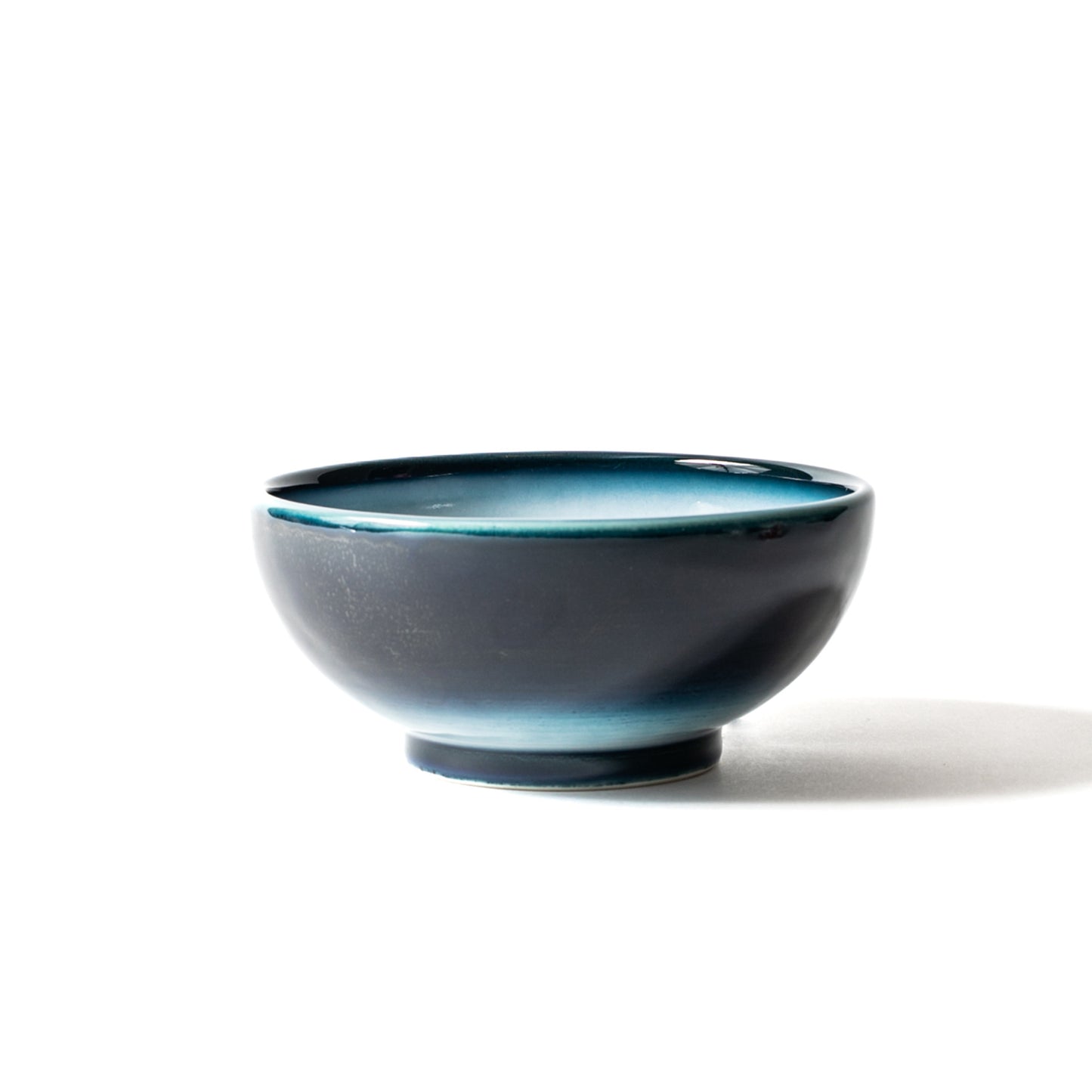 Side view of Shima White donburi bowl—matte exterior navy gradient with luminous white interior rimmed in teal.