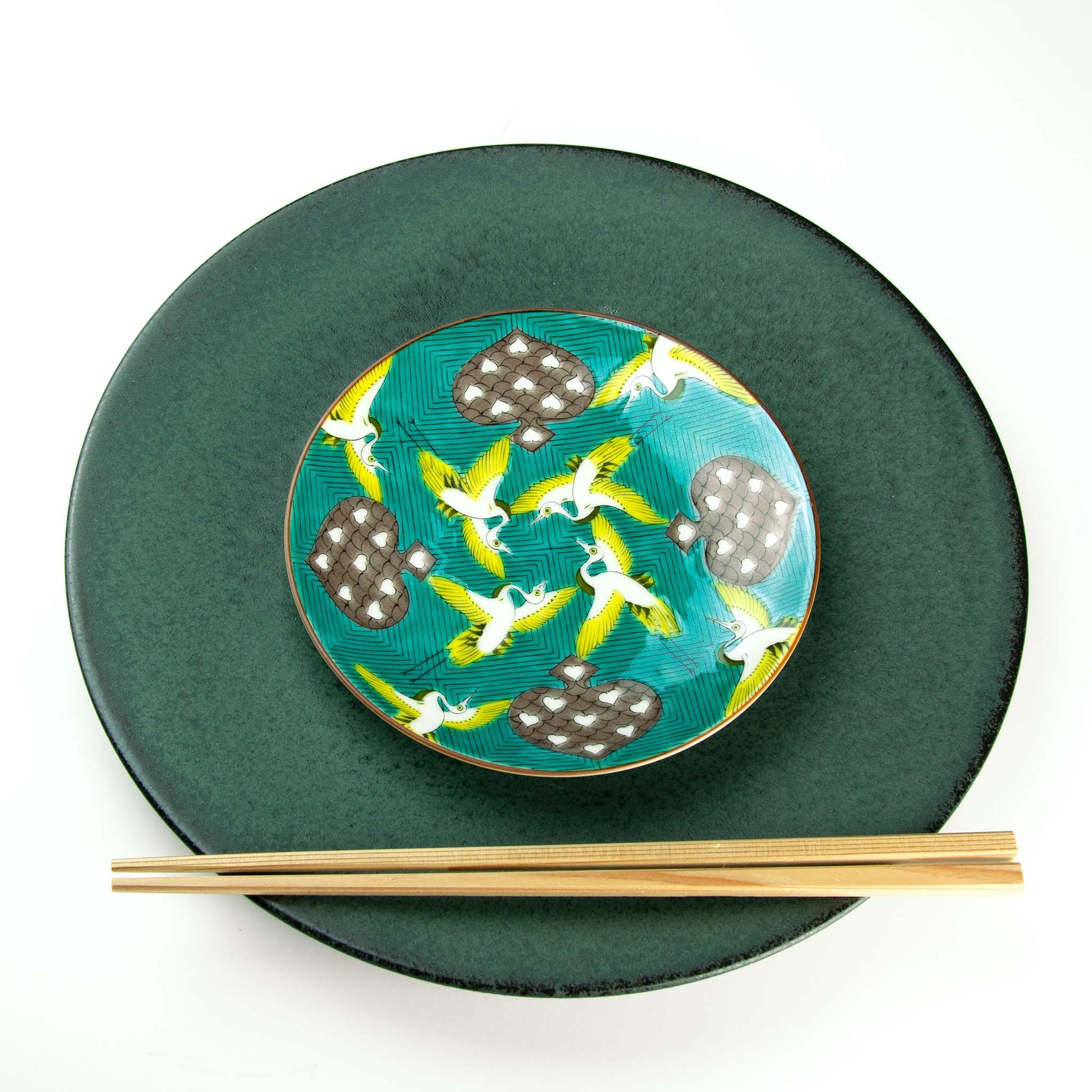 Yellow and white birds flying among spades set on a green background of yellow and blue waves.  Paired with Koku dinnerware.